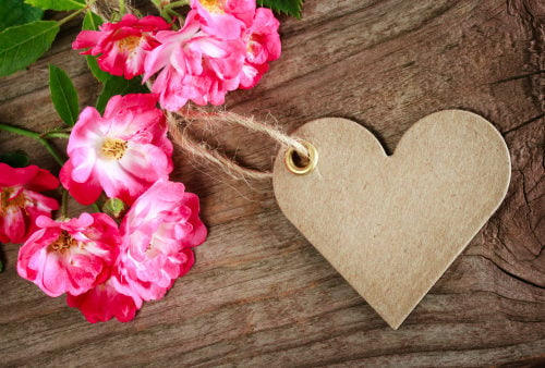 brown heart-shaped gift tag on wooden table with a bouquet of dark pink wild roses