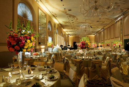 elaborate banquet hall with a large chandalier and many round tables decorated for a wedding dinner