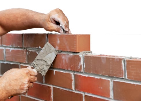 man's hand with trowell constructing a wall of bricks like God is constructing our lives