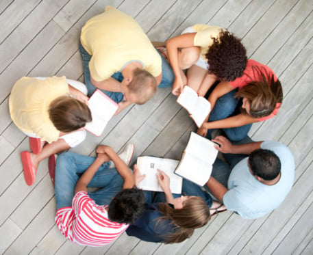 People sitting on ground in a circle studying Bible together about God-Man