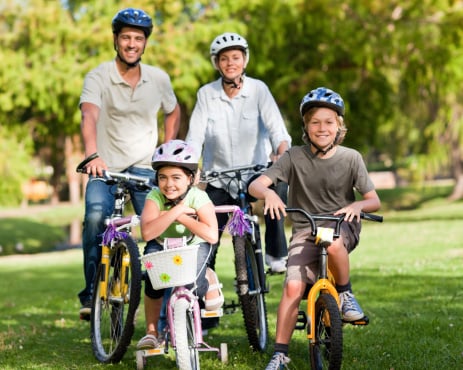 family of four standing with their bicycles outside on a sunny day as they are being active together