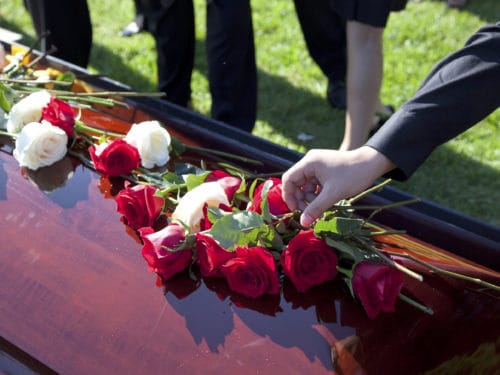 man placing red and white roses on a casket of dead loved one