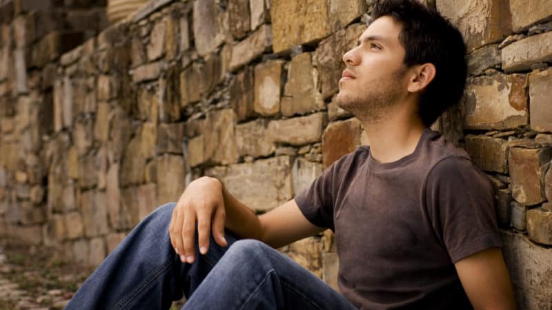 Young man sitting against a stone wall wanting to understand the Bible better