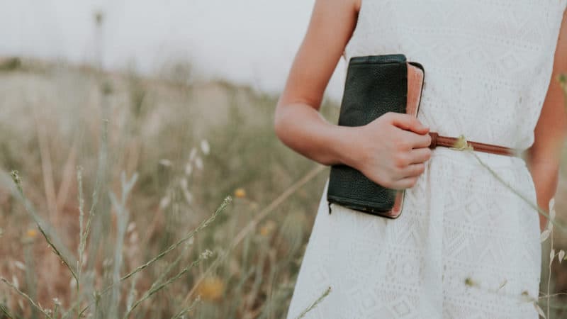 Woman in white dress holding Bible close because she loves the understanding it brings