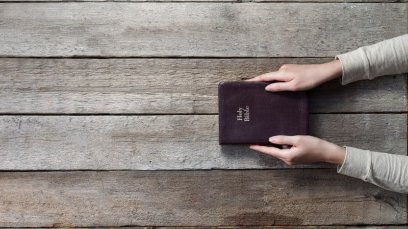 Woman holding closed Bible on a table hoping to find understanding in its pages