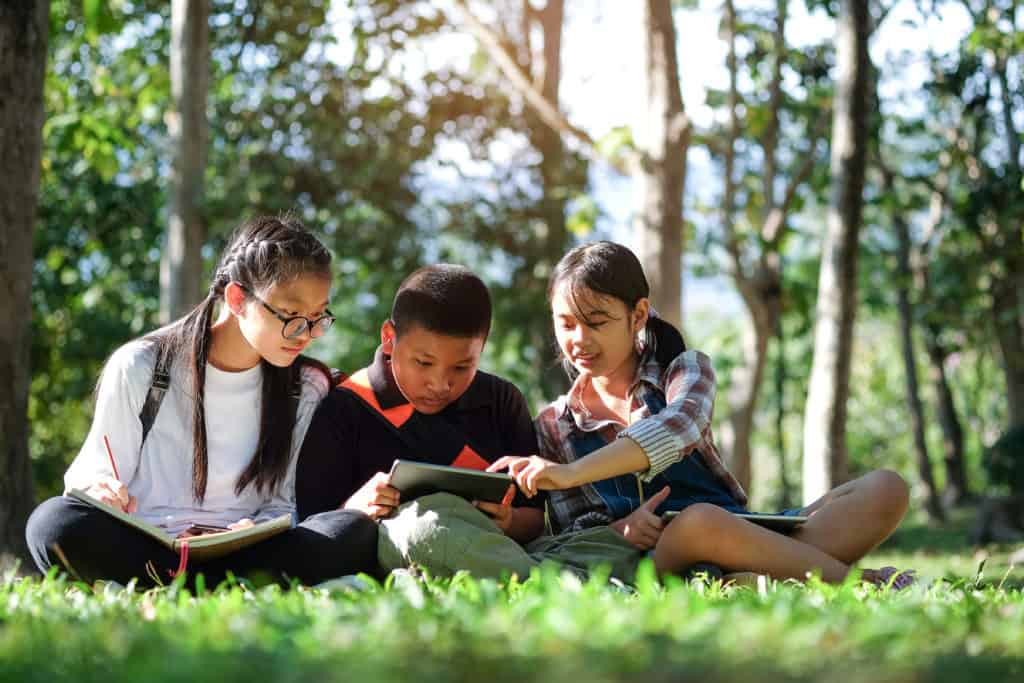 three teens sitting on grass studying how the bible can help them in their daily life