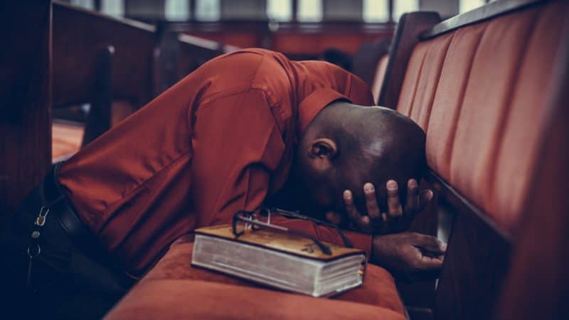 man with Bible kneeling on church pew earnestly in prayer after a bible study