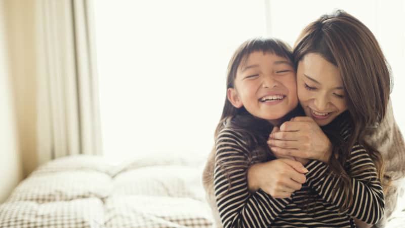 mother and daughter hugging mother and young daughter hugging on a bed on a sunny day