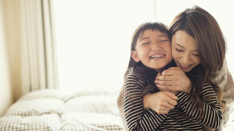 mother and young daughter hugging on a bed on a sunny day