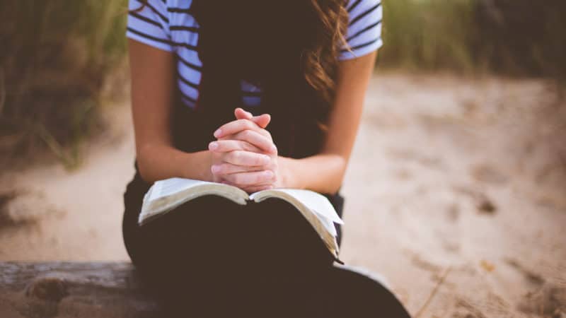 Woman with folded hands on open Bible