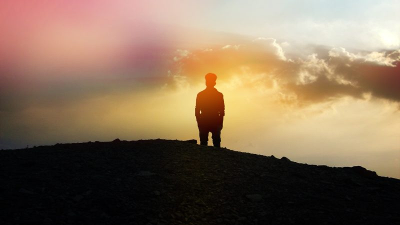 silhouette of man standing on hill at sunset
