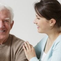 a smiling young woman putting her hand on the shoulder of an older man showing her heart of service