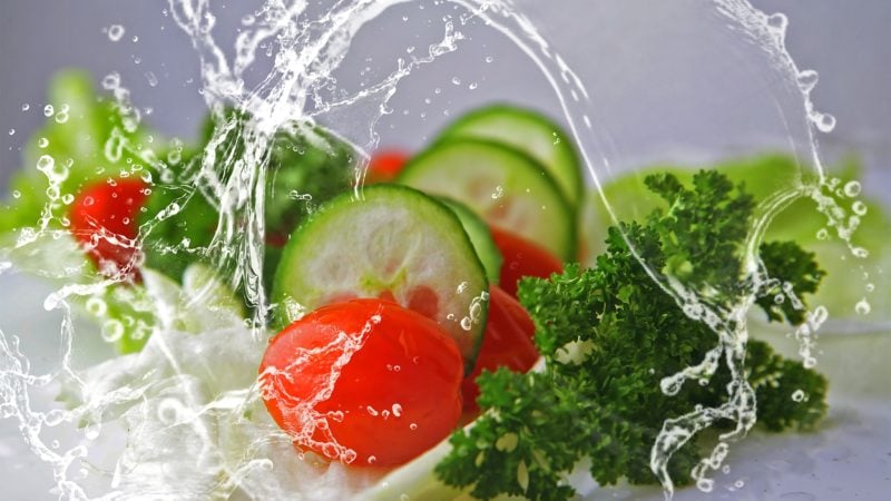 cucumbers, tomatoes, parsley, and lettuce with large splashes of water surrounding them