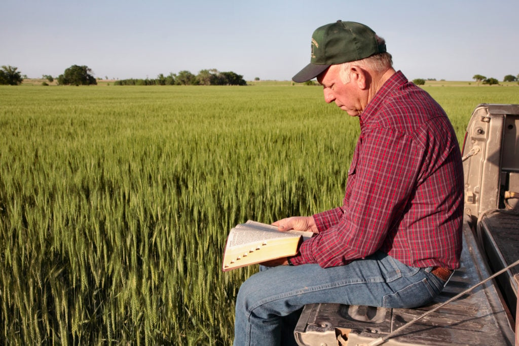 farmer sitting on tailgate of truck in field reading his Bible