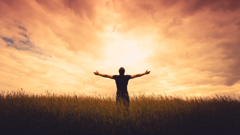 Man standing in field with outstretched arms looking up to heaven