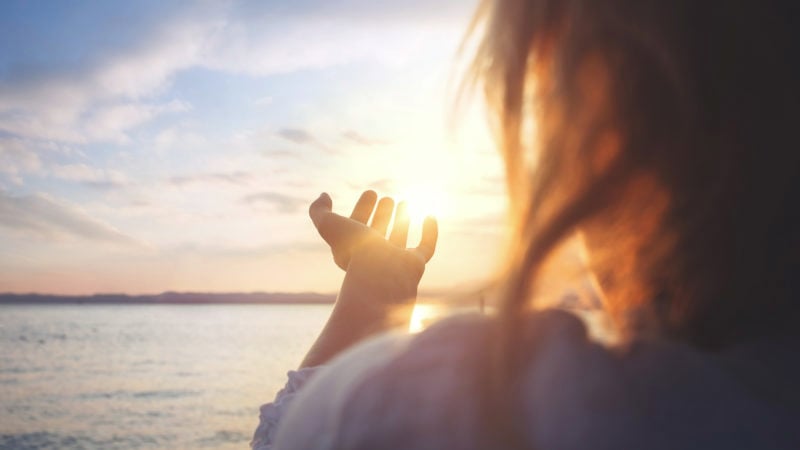 woman at ocean with outstretched hand searching for heaven