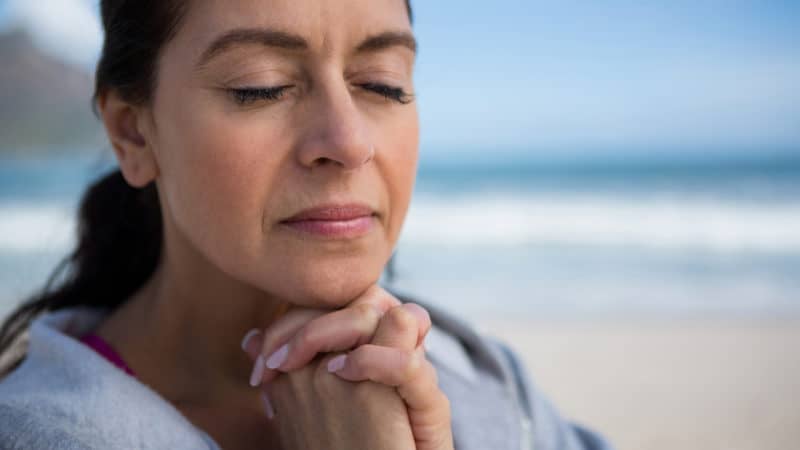 Donna sulla spiaggia che prega per una migliore comprensione dei profeti 