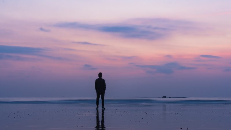 Homem na praia após o pôr do sol, pensando no que fazer um profeta