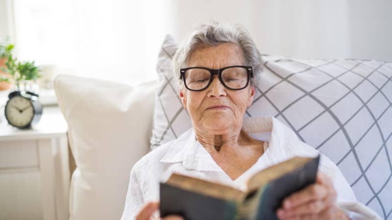 older woman lying in bed reading bible