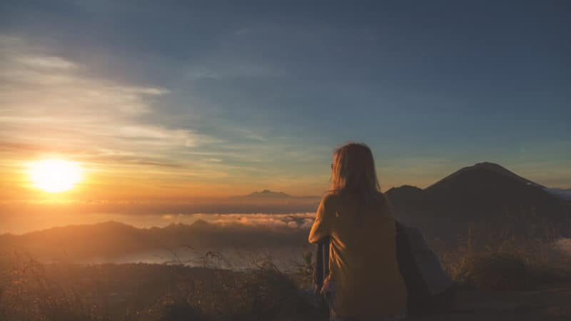 woman sitting on top of a mountain overlooking a valley at sunset and feeling close to God