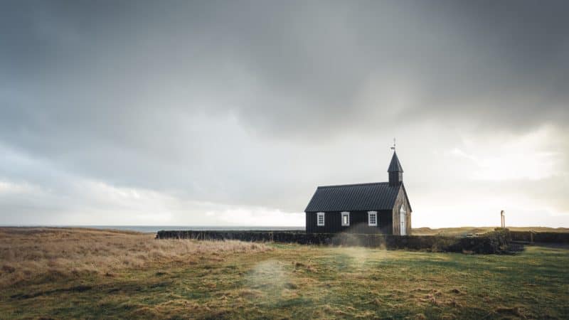 small brown church alone in a field surrounded by a hedge 