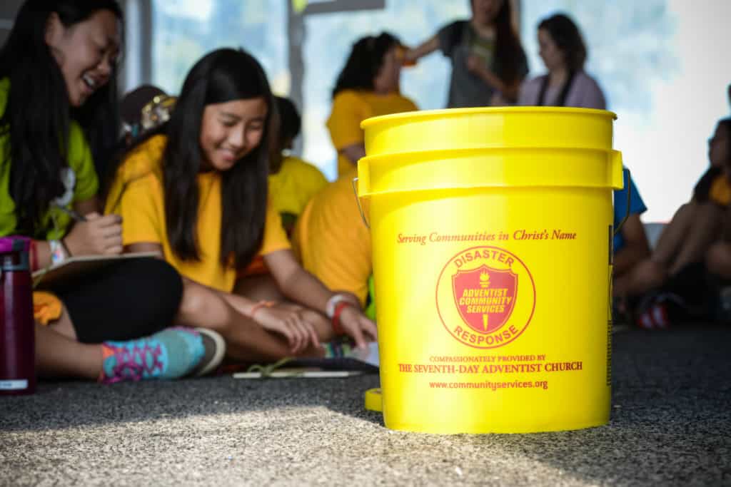 Adventist community services yellow bucket in the midst of youth volunteers