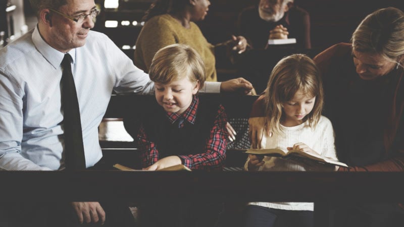 Family sitting together in church pew on Sabbath reading the Bible