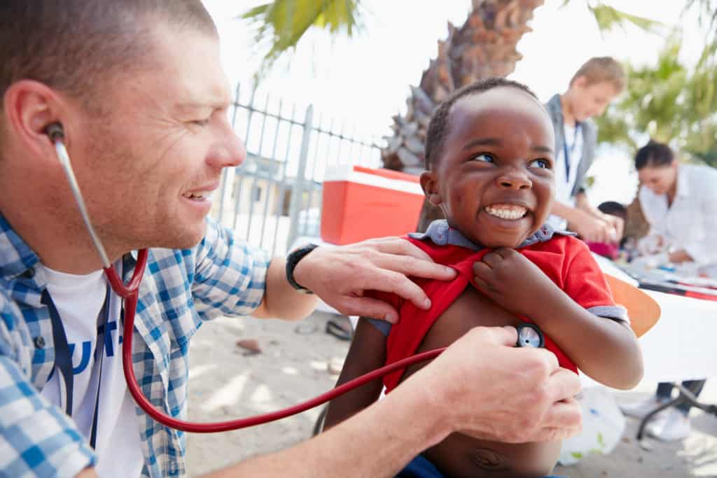 volunteer helping young boy Adventist medical volunteer using stethoscope on smiling young boy