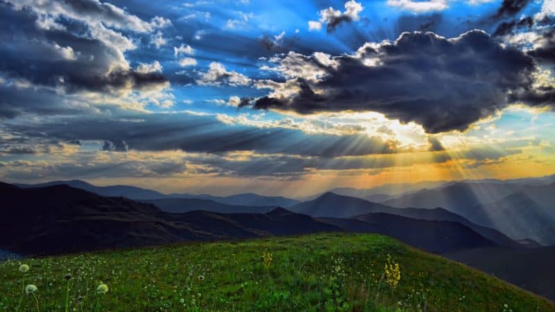 sun beams shining through clouds in heavens over alpine meadow