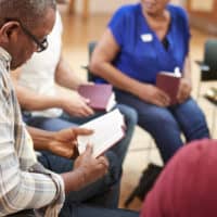 A man in a circle with friends reading from his bible.