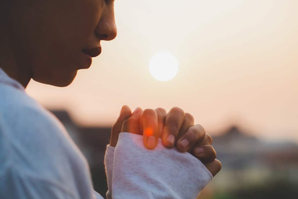 Person praying to give thanks for God’s blessings during the week at sunset.