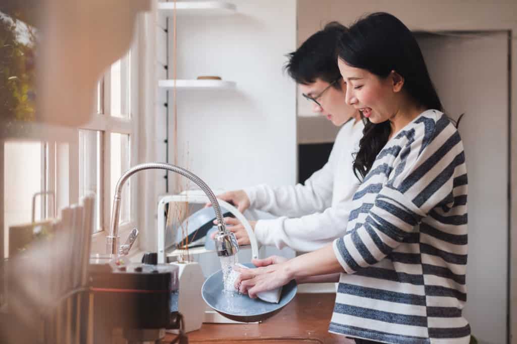 Young family couple washing dishes together to prepare on Friday afternoon for Sabbath.