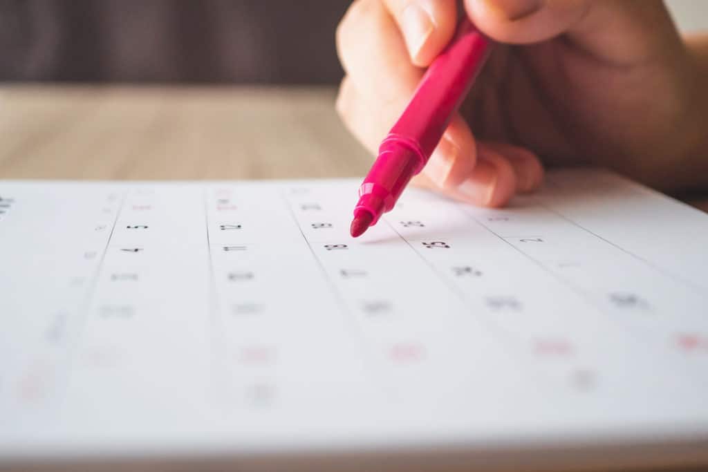 Hand with pen counting the week days until Saturday on a calendar.