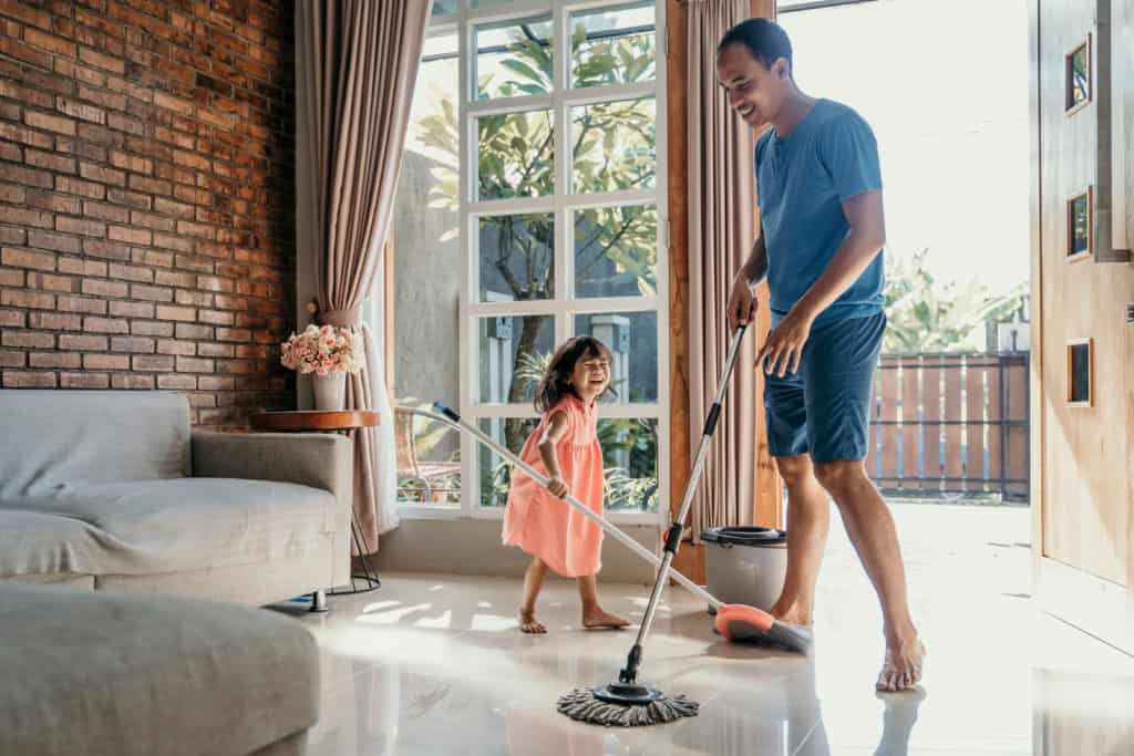 father and young daughter laughing while they sweep and mop to get ready to celebrate the Sabbath