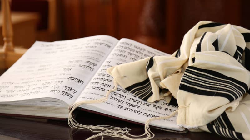 black and white Jewish prayer shawl draped over open bible written in Hebrew text symbolizing the sabbath throughout history