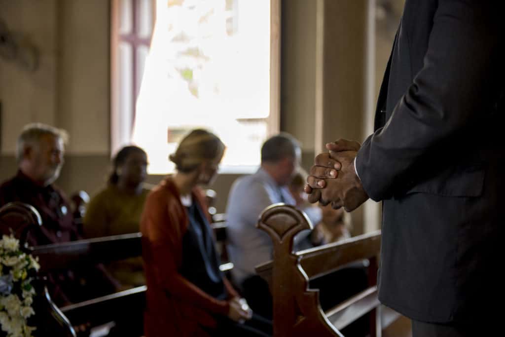 African American pastor standing in front of small congregation sitting in wooden church pews on Sabbath
