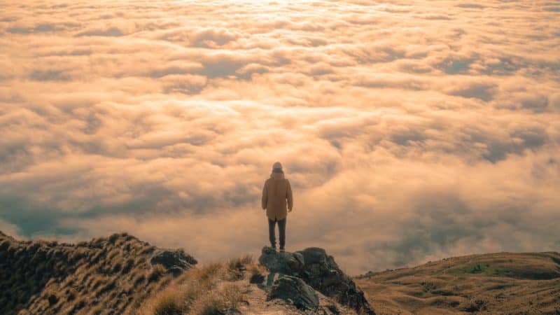 Person standing on a mountain looking out over the clouds, similar to how Moses climbed the mountain of God to talk with Him.