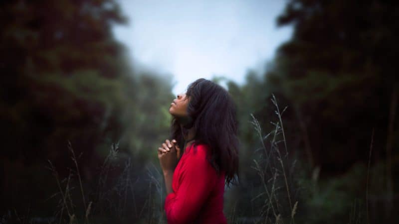 Beautiful woman standing in a forest with her head raised and praying
