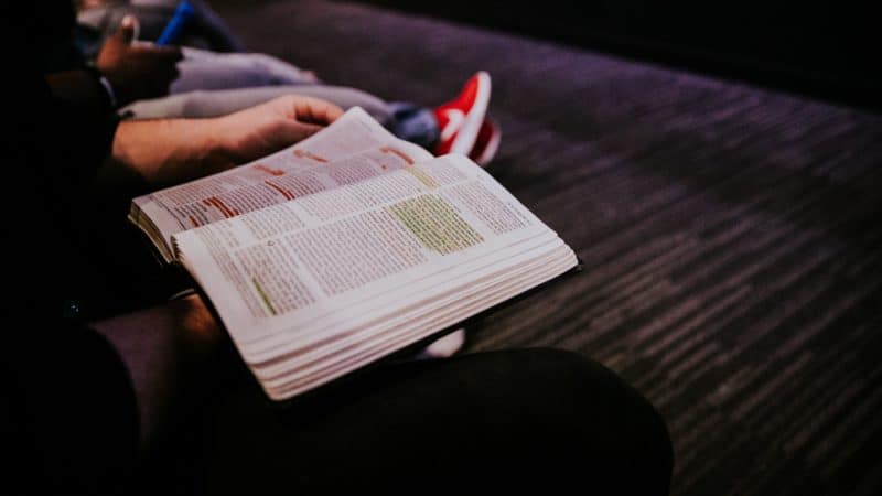 Person sitting studying a highlighted Bible, to better understand God’s Word.