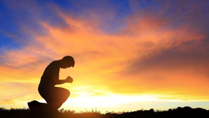 silhouette of man kneeling and praying during beautiful sunset at the close of the Sabbath