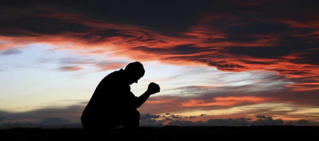 Silhouette of man kneeling and praying at sunset to open the Sabbath.