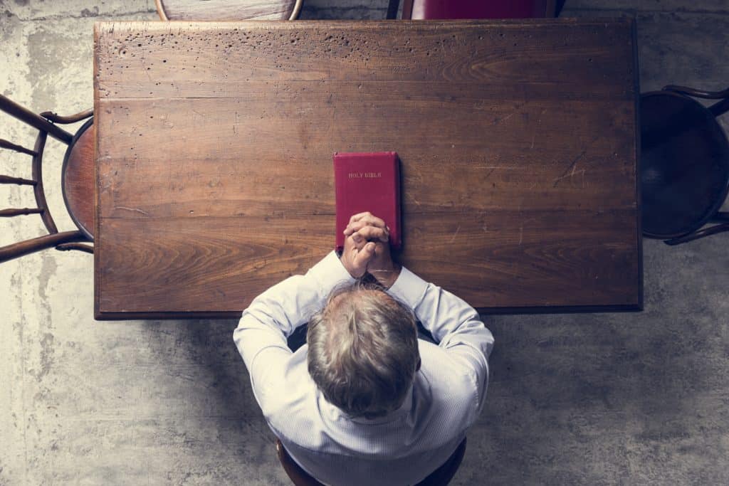 Senior man sitting a table, praying with a Bible 