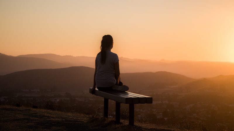 Woman sitting on a bench looking at hills at sunset