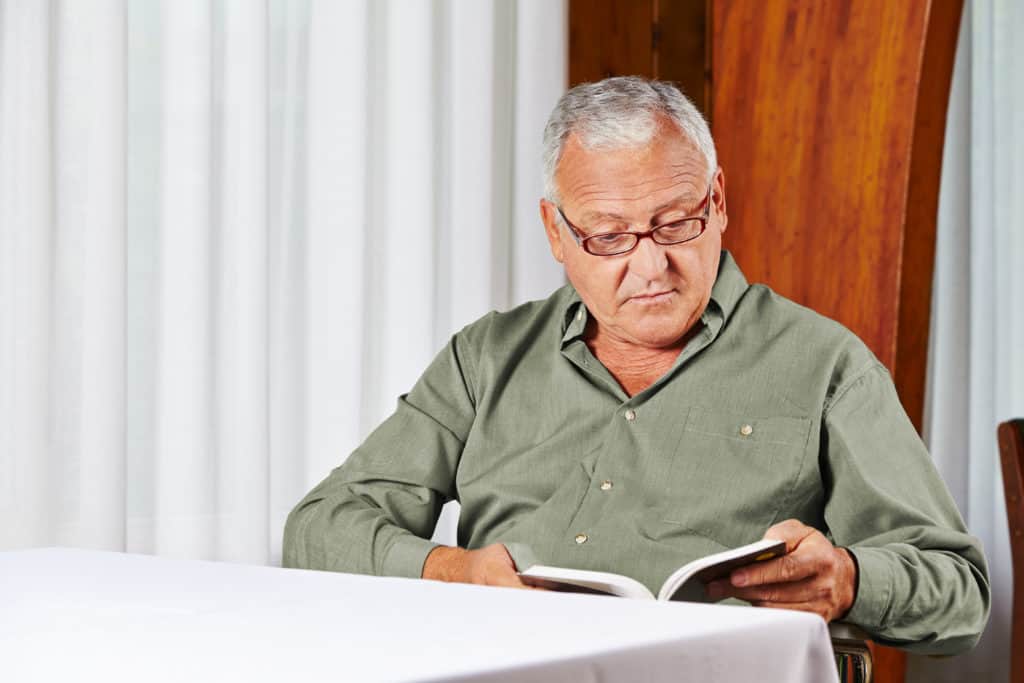 Senior man in rest home reading a book with reading glasses