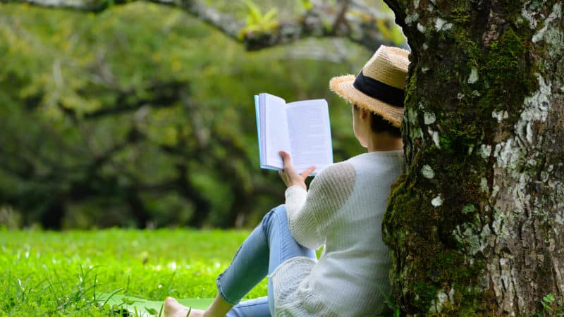 Middle aged woman sitting under a tree reading a book in the park