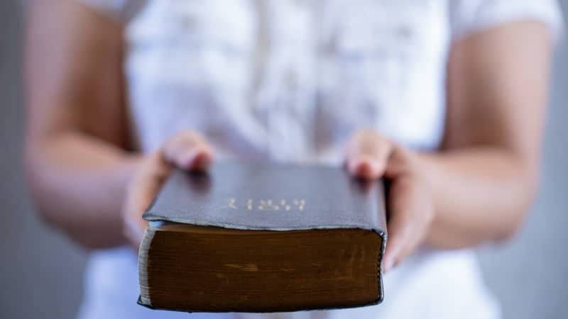 Person holding out bible towards the viewer. 