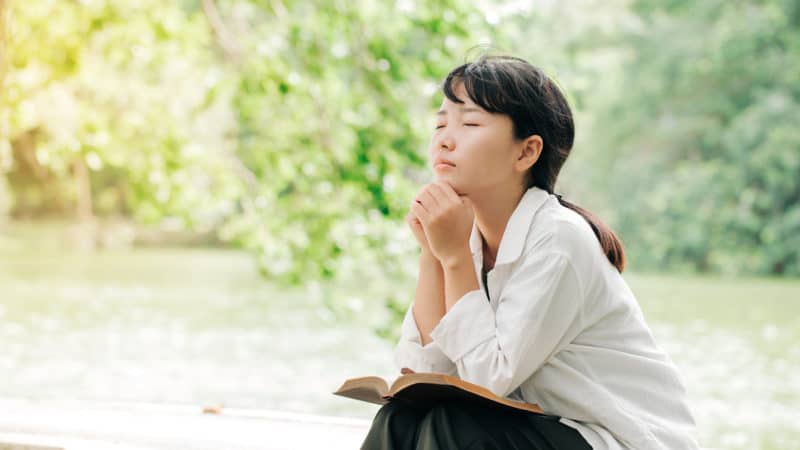 Woman praying in the morning on nature background. Hands folded in prayer on a Bible as we learn nature of humanity