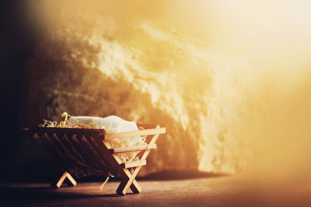 Wooden manger with cloth and hay inside, a rock wall set in the background. 