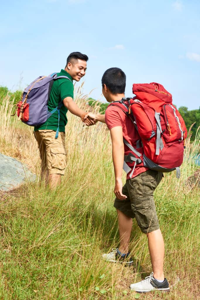 Smiling hiker outstretching hand to help his friend