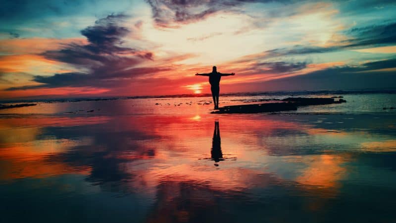 silhouette of a woman on the beach with arms outstretched in front of a vibrant red sunset 